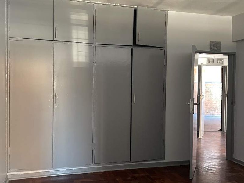A bedroom featuring classic parquet flooring and extensive built-in cupboard storage with overhead cabinets.