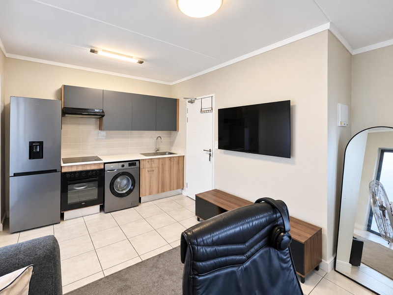 Modern open-plan living area featuring a compact kitchen with built-in cabinetry, integrated appliances, and tiled flooring, seamlessly connected to the living space.