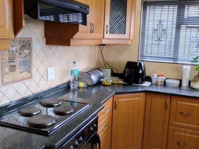 A functional kitchen featuring wood-look laminate cabinetry, dark granite countertops, an integrated electric hob and oven, and classic tiled flooring.