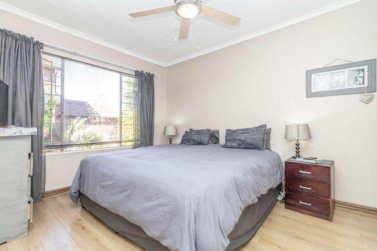 A well-lit bedroom featuring light wood-look flooring, a ceiling fan, and large windows with fitted blinds.