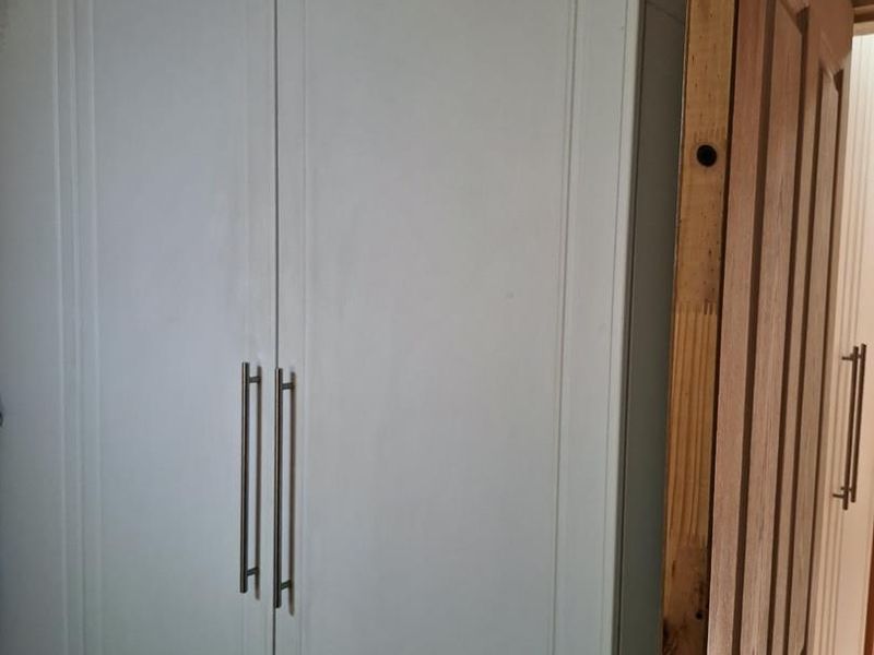 A close-up view of a built-in wardrobe with white doors and an adjacent timber door showing unfinished edges.