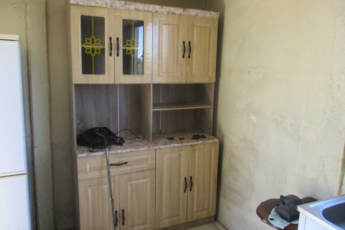 A kitchen area featuring built-in wooden cabinetry with laminate countertops and tiled flooring, set against an unfinished wall surface.