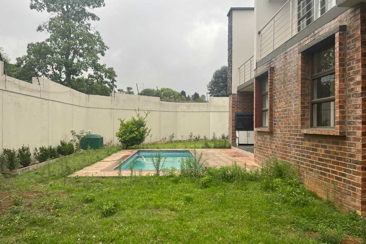 Rear garden area featuring a small swimming pool, paved surround, and perimeter walling, adjacent to the brick-clad rear elevation of the property.