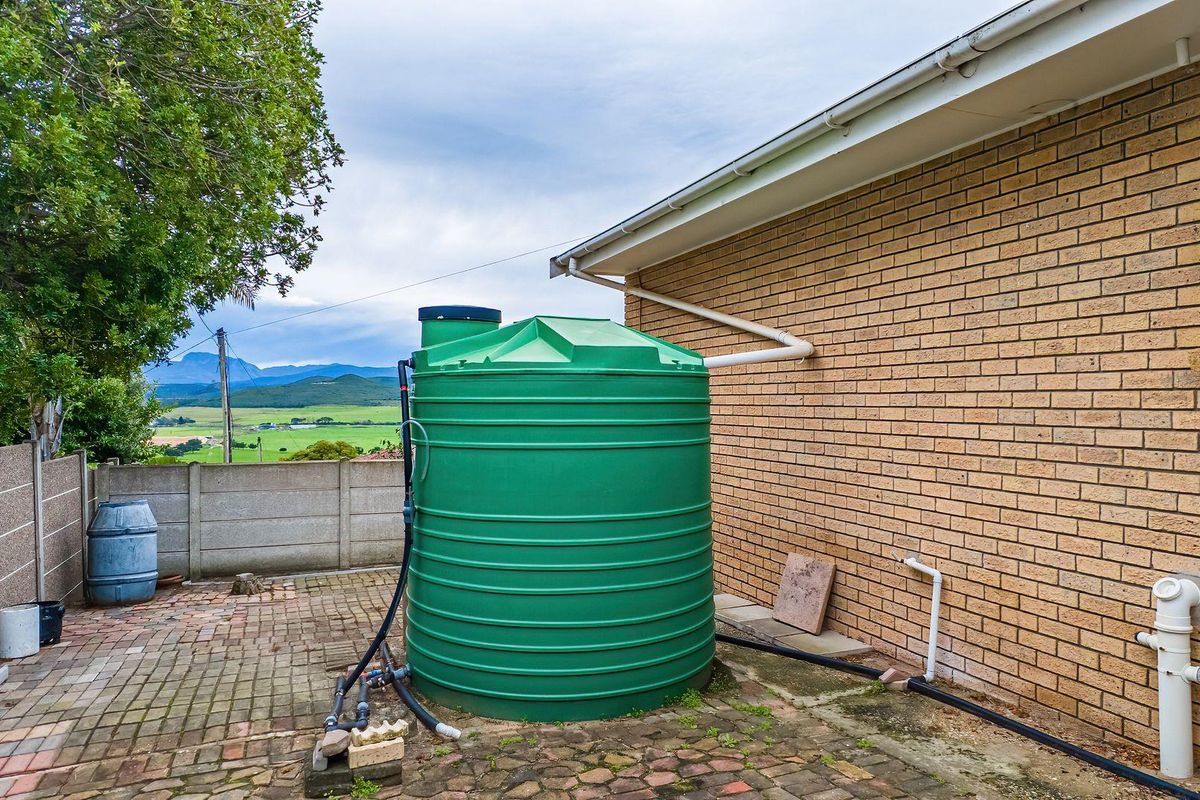 Exterior rear area featuring a large green water storage tank connected to the roof guttering system, set on a paved courtyard.