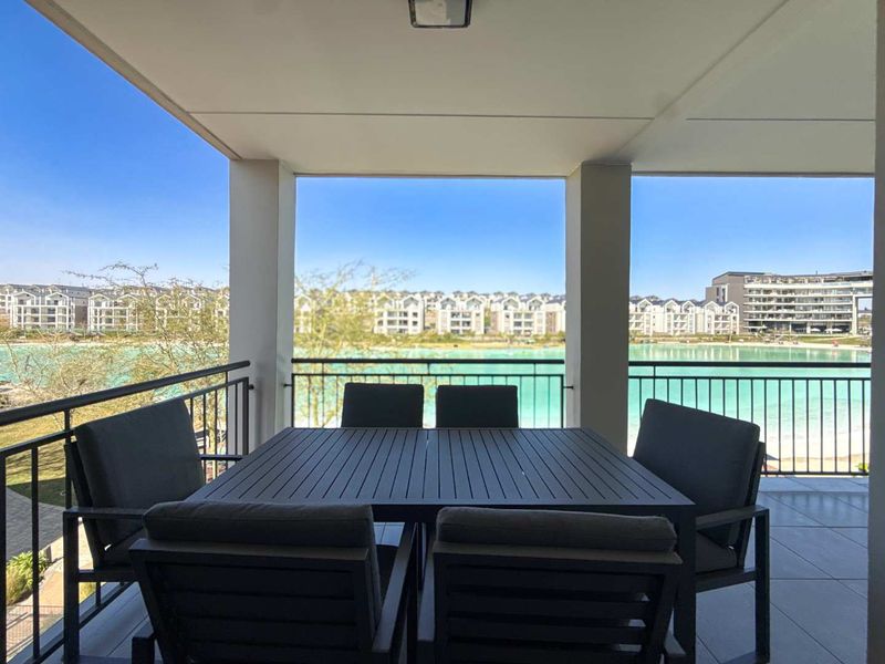 A covered balcony featuring tiled flooring and a metal balustrade, offering scenic views of the surrounding estate and water feature.