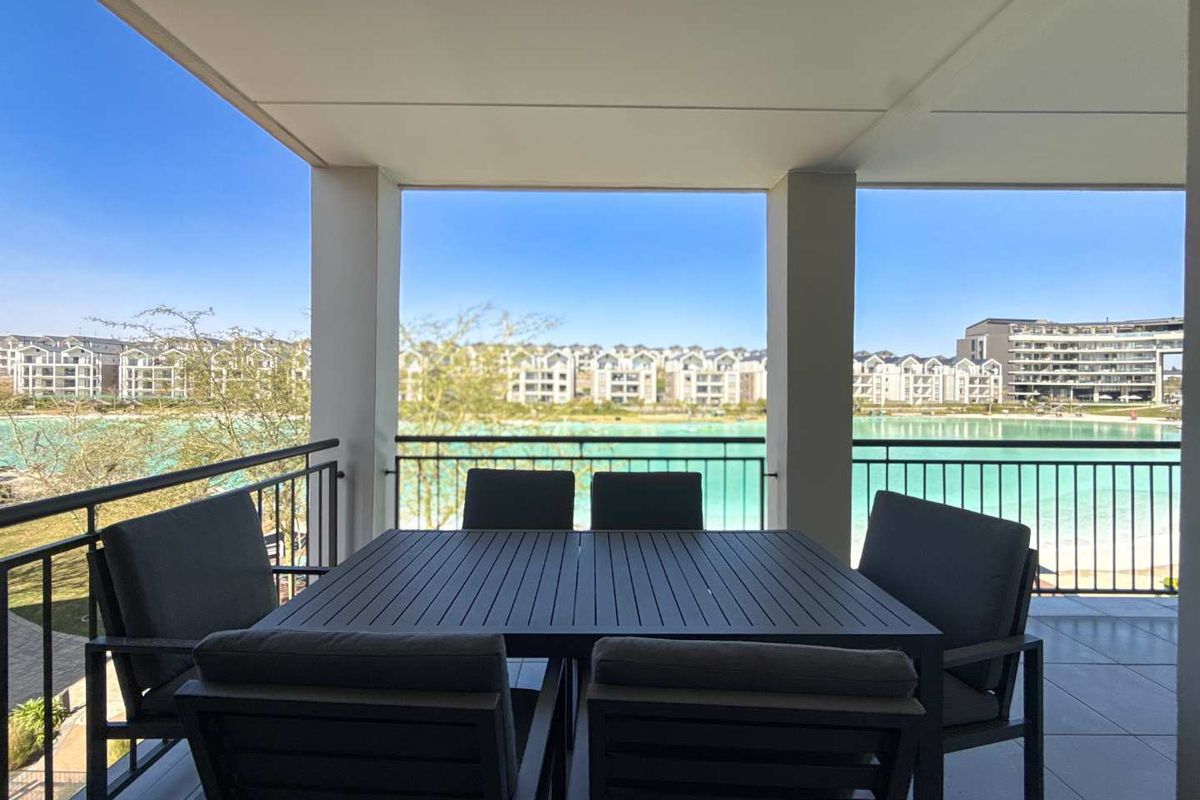 A covered balcony featuring tiled flooring and a metal balustrade, offering scenic views of the surrounding estate and water feature.