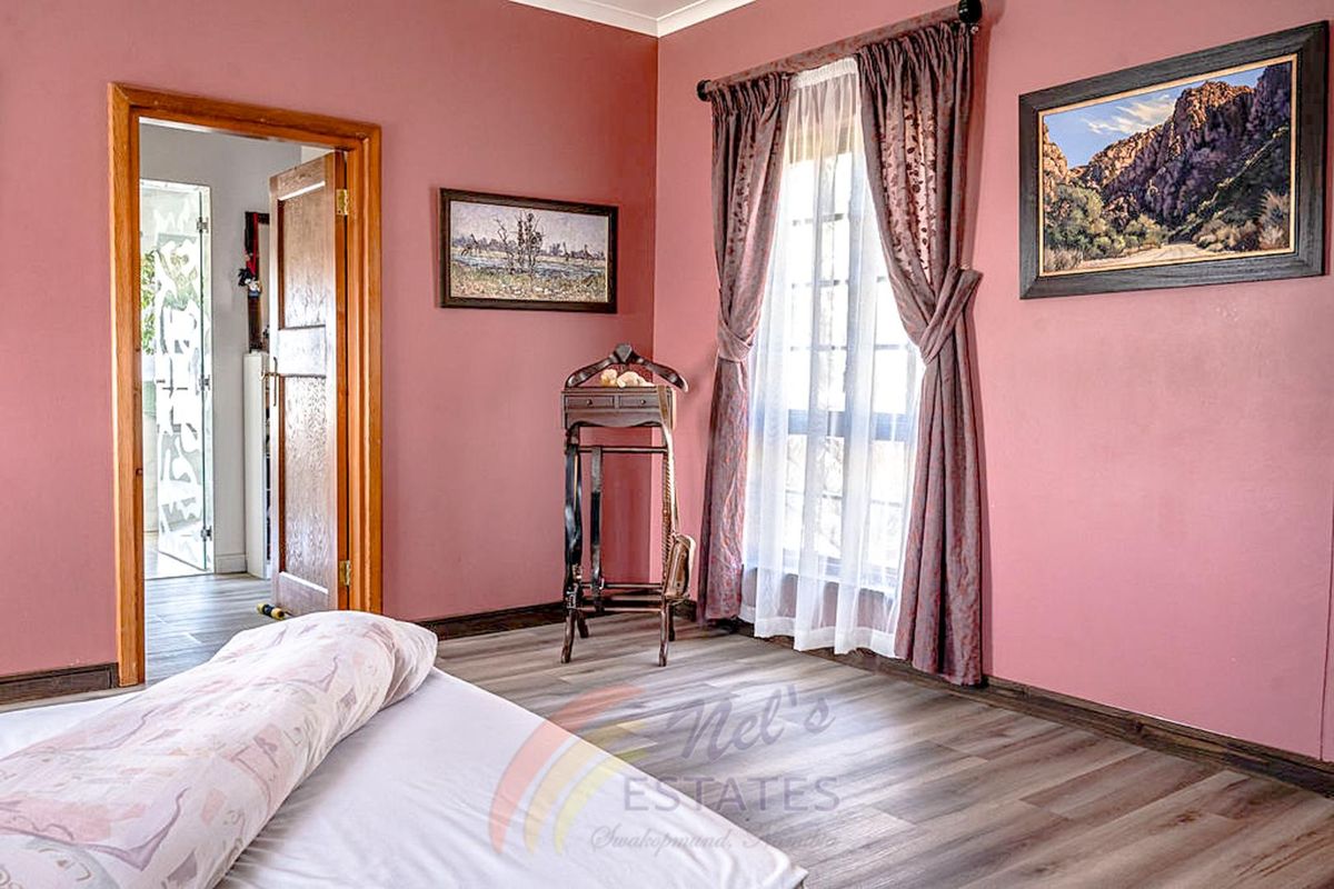 A bedroom featuring wood-look laminate flooring, timber door frames, and a window with curtains, providing a functional living space.