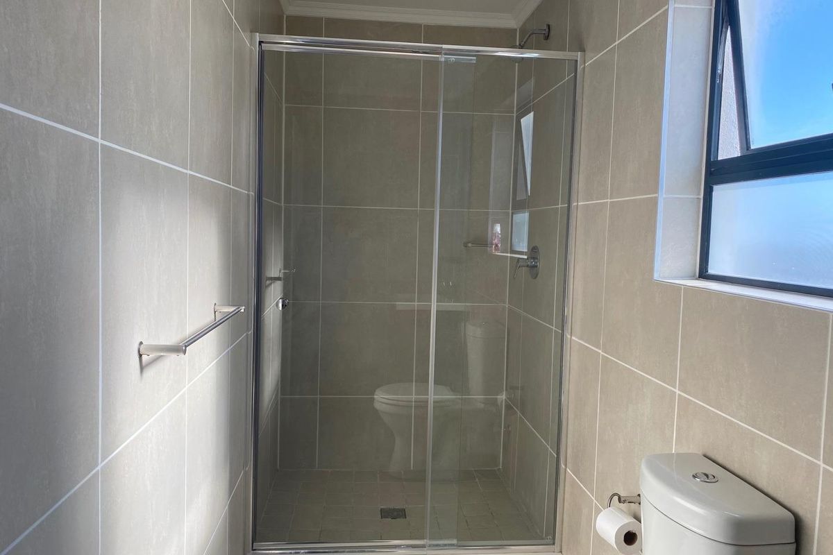 A modern bathroom featuring a glass-enclosed shower with neutral wall tiling and a standard toilet.