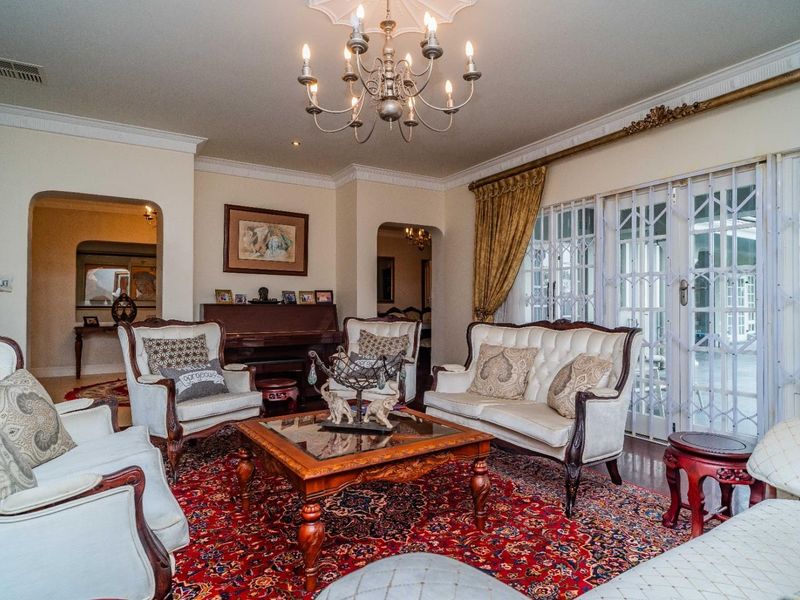 Spacious living room featuring classic architectural details, including a decorative ceiling rose, ornate chandelier, and sliding glass doors with security gates leading outdoors.
