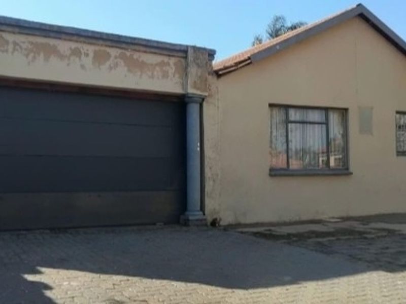 Front elevation of a house featuring a large garage door, paved driveway, and tiled roof, showing signs of exterior wear and paint deterioration.