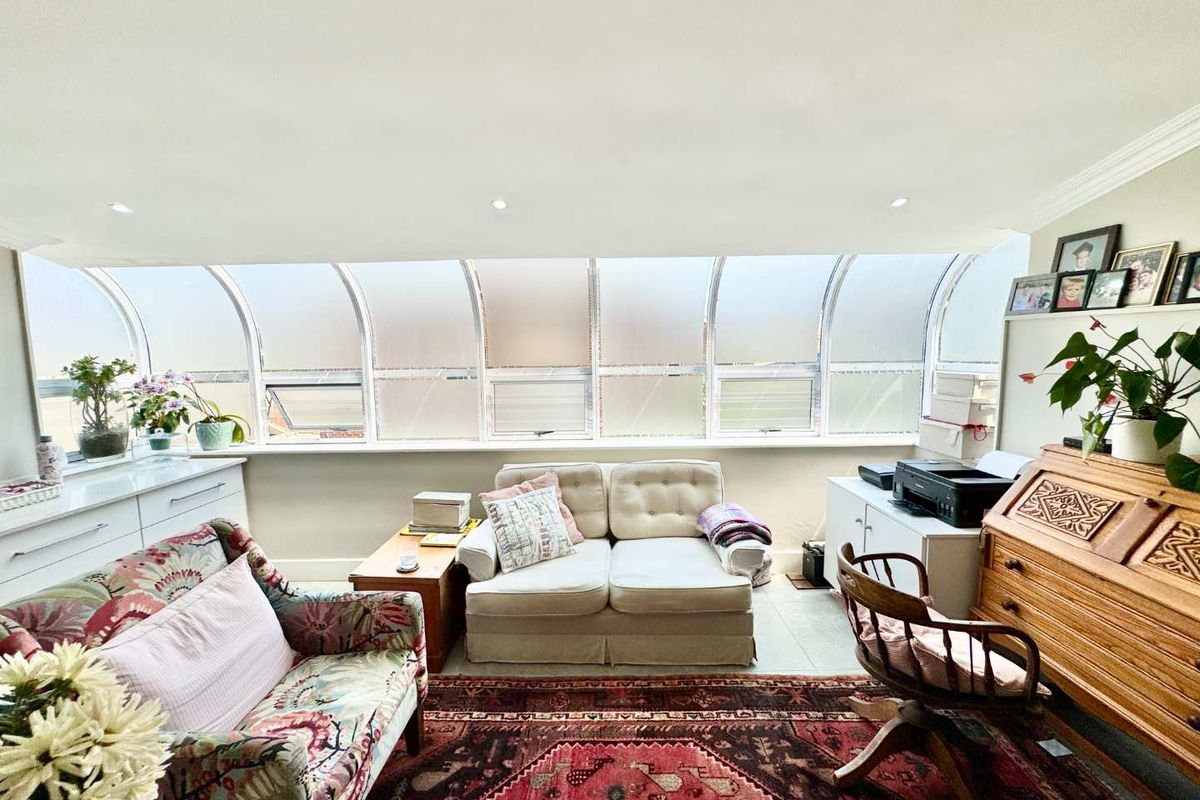 A sun-drenched living area featuring a unique curved glass window wall, recessed ceiling lighting, and tiled flooring, offering a bright and versatile space.