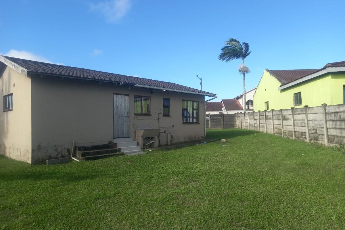 Rear view of the property featuring a large grass lawn, concrete boundary wall, and exterior utility sink attached to the house structure.