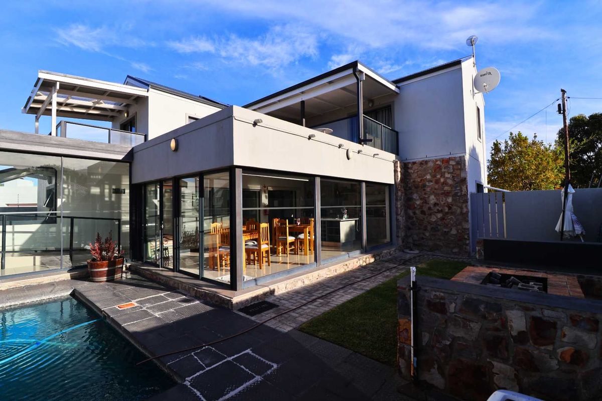 Rear view of the property featuring a swimming pool, stone-clad exterior walls, large glass sliding doors, and an upper-level balcony.
