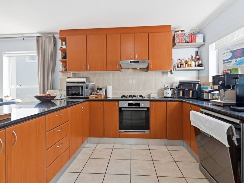 A functional kitchen featuring warm-toned laminate cabinetry, granite countertops, a gas hob, and a built-in oven with tiled flooring and backsplash.