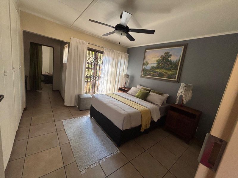 A spacious bedroom featuring tiled flooring, a ceiling fan, and built-in cupboards, with direct access to an outdoor area through a security gate.