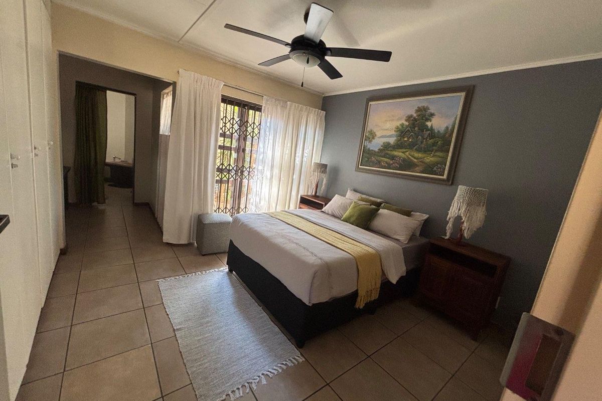 A spacious bedroom featuring tiled flooring, a ceiling fan, and built-in cupboards, with direct access to an outdoor area through a security gate.
