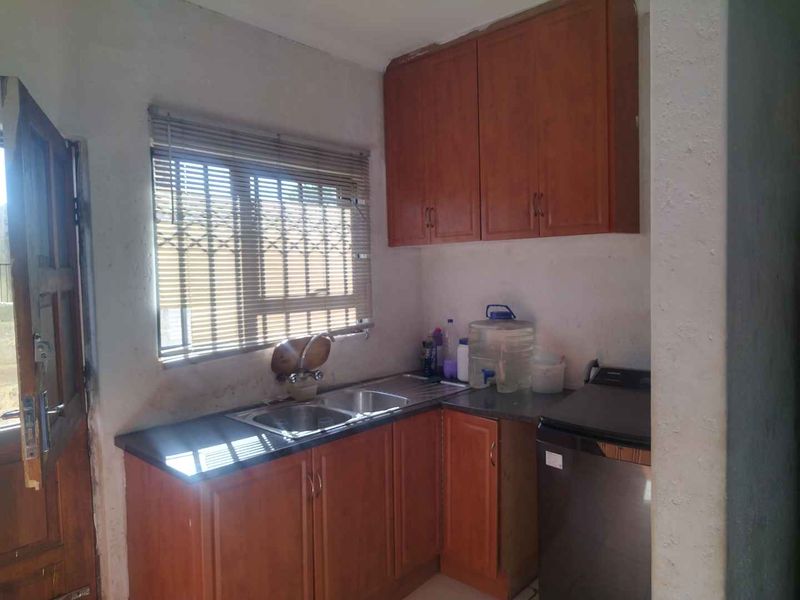 A compact kitchen area featuring wooden cabinetry, a double bowl sink, and a window with venetian blinds, providing a functional prep space.