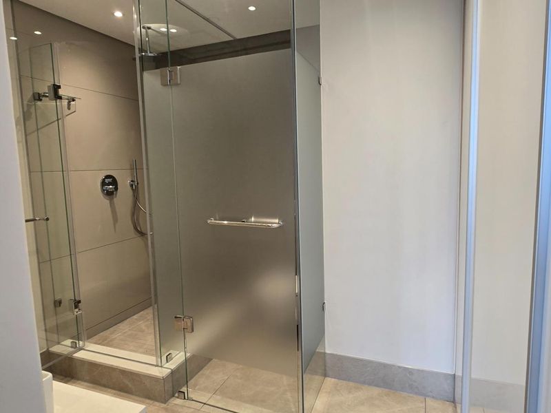 A modern, well-maintained bathroom featuring a glass-enclosed shower with a frosted door and contemporary tiled finishes.