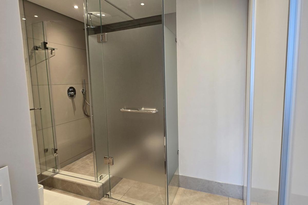 A modern, well-maintained bathroom featuring a glass-enclosed shower with a frosted door and contemporary tiled finishes.
