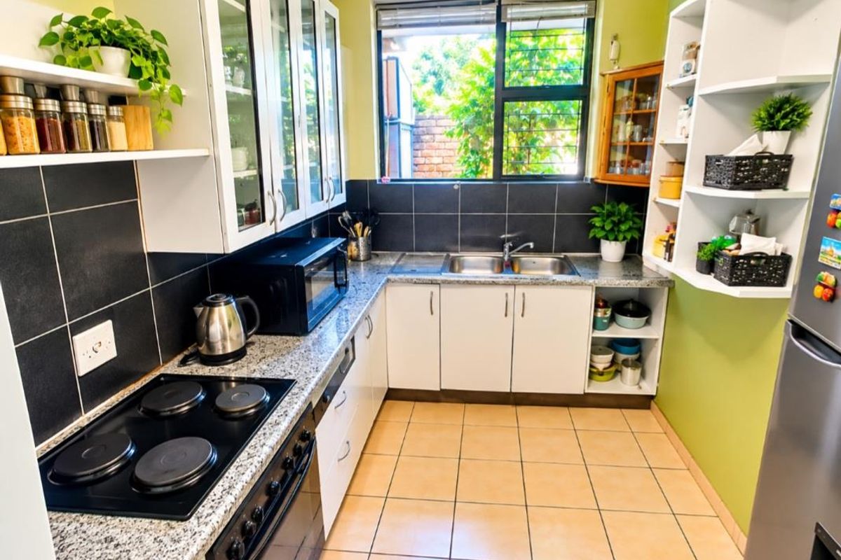 A functional kitchen featuring white cabinetry, granite countertops, a double basin sink, and a built-in electric hob and oven with tiled backsplash.