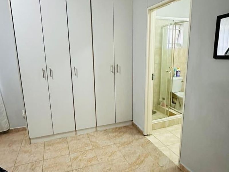 A clean, empty bedroom featuring built-in cupboards, tiled flooring, and direct access to an en-suite bathroom.