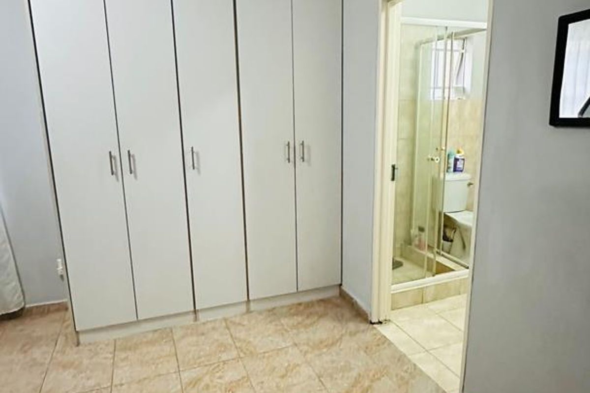 A clean, empty bedroom featuring built-in cupboards, tiled flooring, and direct access to an en-suite bathroom.