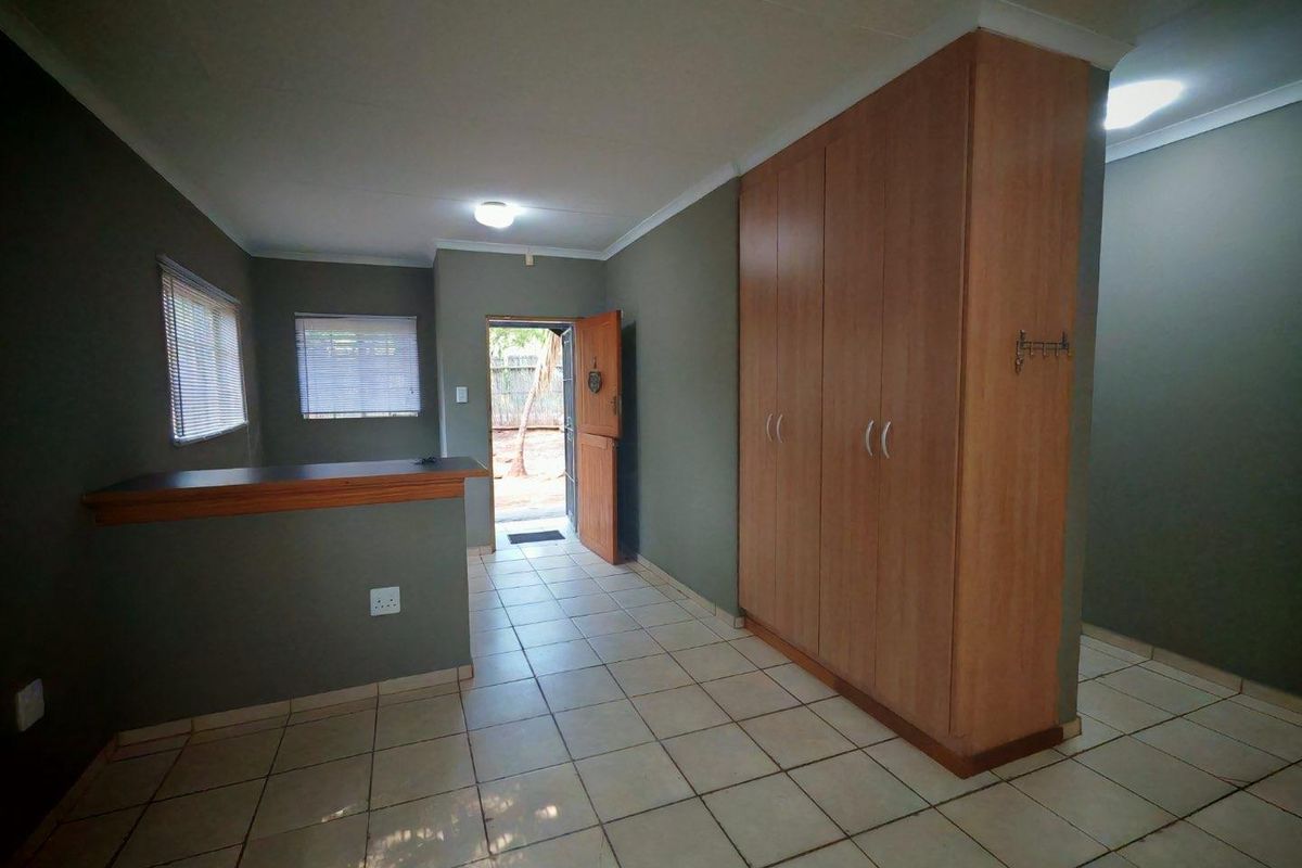 A spacious bedroom featuring tiled flooring, built-in cupboards, and a breakfast bar counter, with direct access to the exterior.