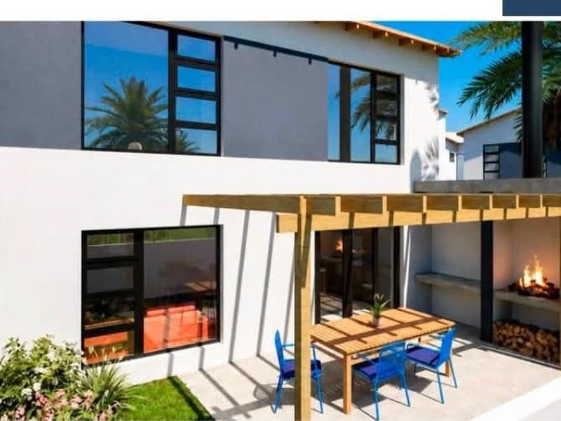 Rear exterior view of a modern townhouse featuring a paved patio, timber pergola, and a built-in braai area.
