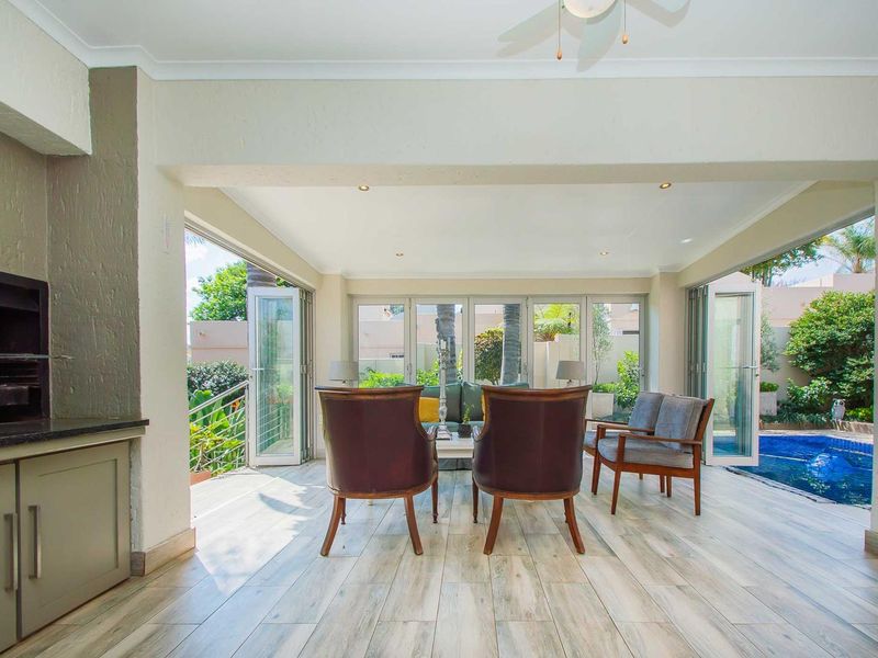 Spacious covered patio featuring a built-in braai, modern tiled flooring, and large bi-fold doors opening directly onto the pool area.