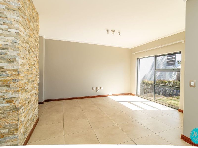 Bright and spacious living area featuring a decorative stone feature wall, large sliding glass doors, and neutral tiled flooring.