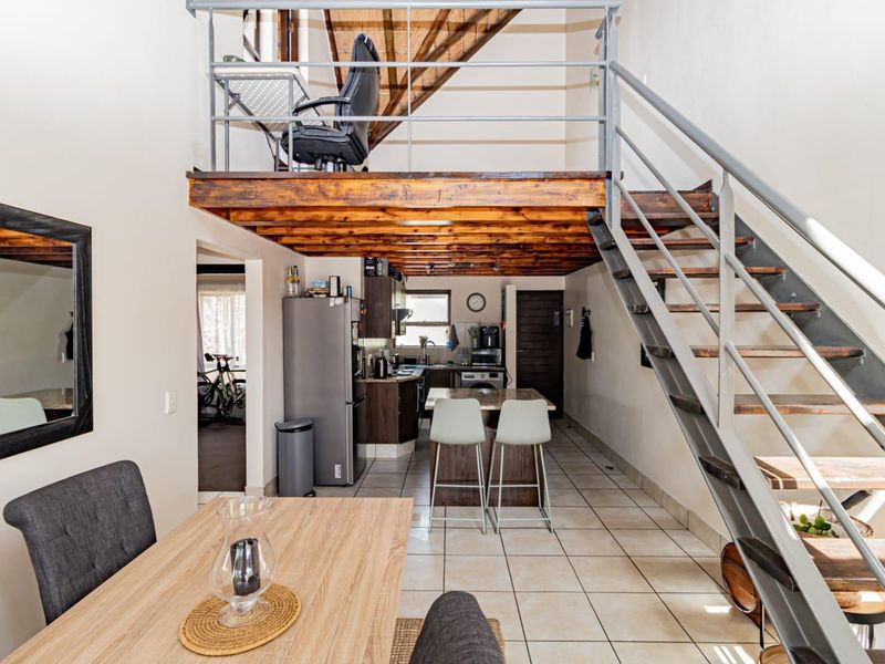 Open plan living area featuring a mezzanine level, metal staircase, tiled flooring, and a functional kitchen with built-in cabinetry and island.