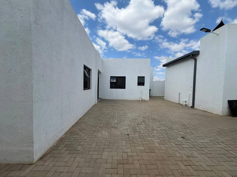 A clean, paved rear courtyard area featuring white textured exterior walls and modern aluminium window frames, offering a low-maintenance outdoor space.