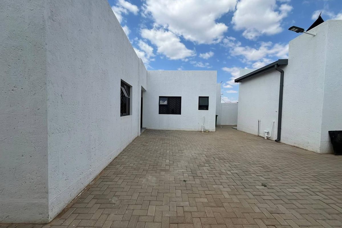 A clean, paved rear courtyard area featuring white textured exterior walls and modern aluminium window frames, offering a low-maintenance outdoor space.