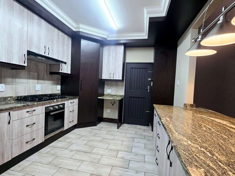 Modern kitchen featuring granite countertops, built-in oven, gas hob, extractor fan, and ample cabinetry with a clean, contemporary finish.