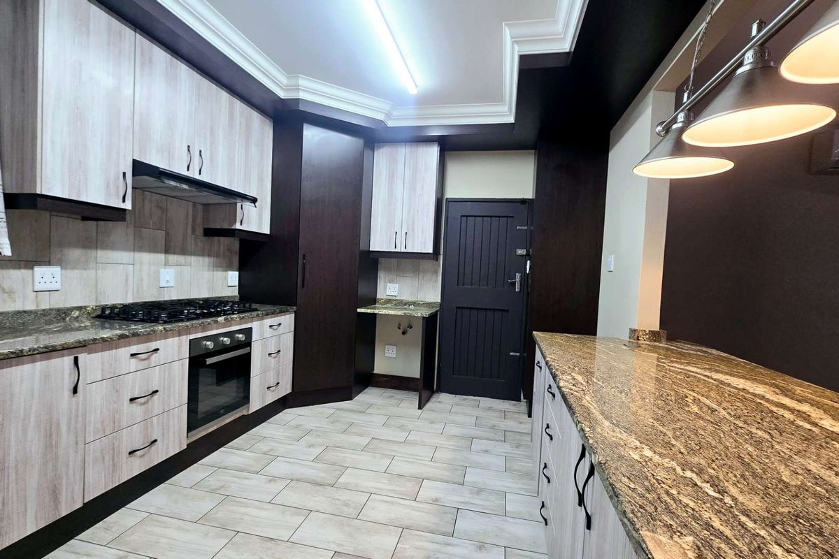 Modern kitchen featuring granite countertops, built-in oven, gas hob, extractor fan, and ample cabinetry with a clean, contemporary finish.