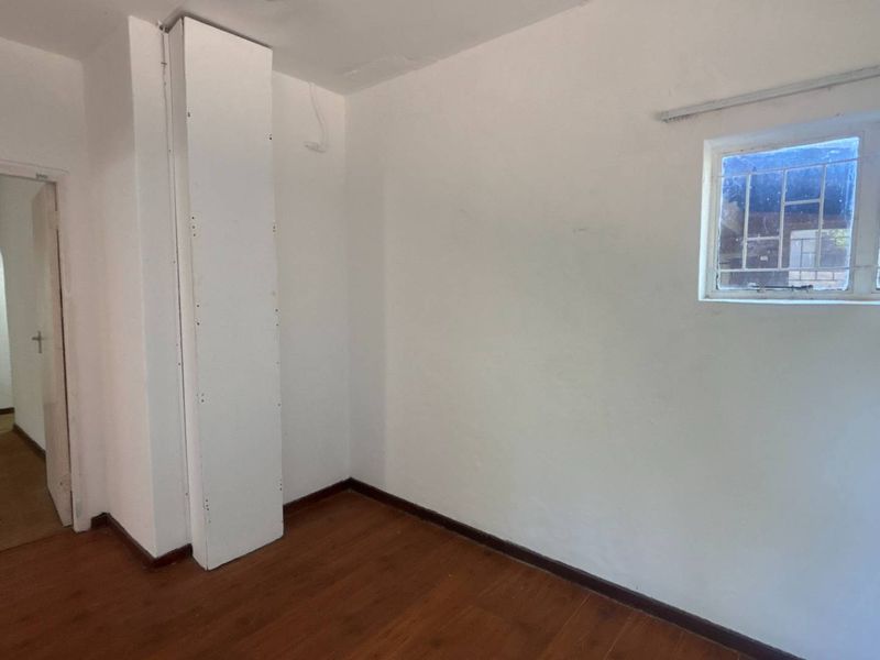 An empty bedroom featuring laminate flooring, a built-in cupboard, and a window with security bars, requiring minor cosmetic repairs.