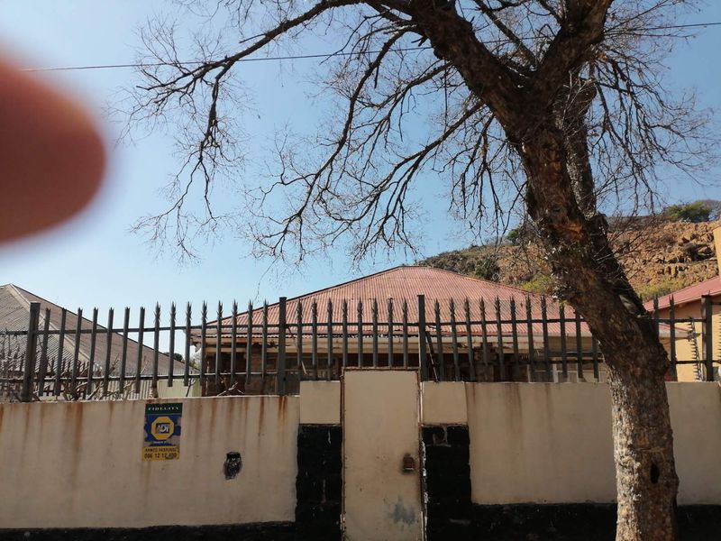 Front view of the property featuring a perimeter wall with metal spike fencing and a corrugated metal roof.