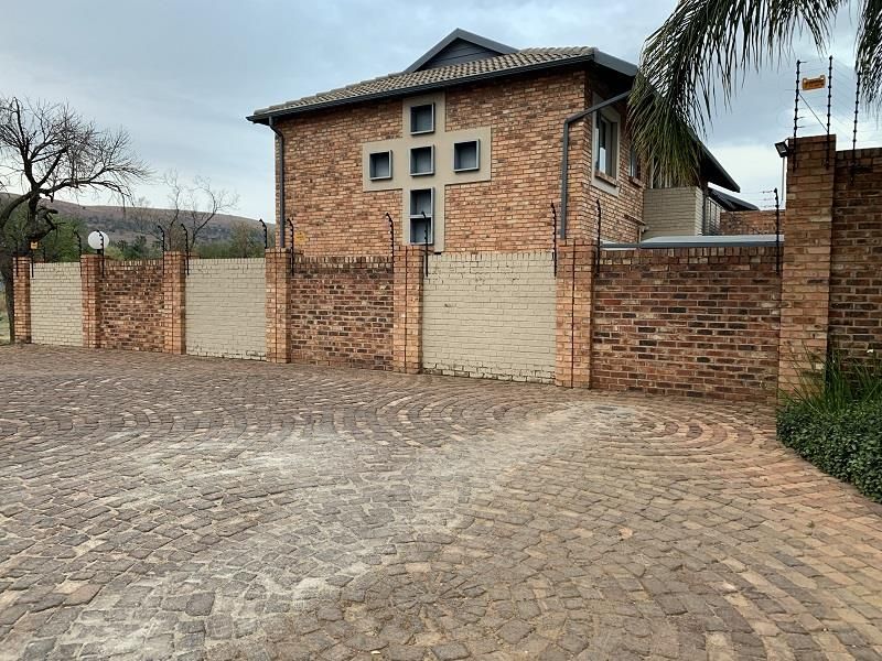 A view of the townhouse exterior featuring a facebrick facade, secure boundary wall with electric fencing, and a paved cobblestone driveway.