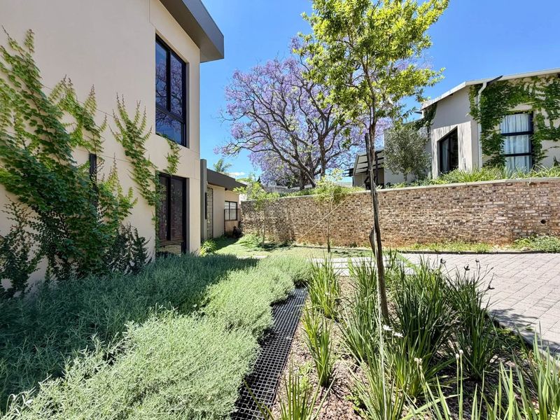 A well-maintained rear garden area featuring a stone retaining wall, paved driveway, and established landscaping alongside the modern building exterior.