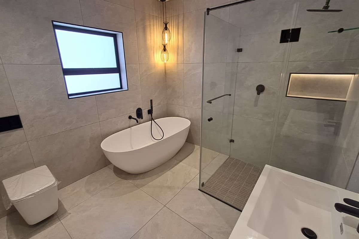 Modern bathroom featuring a freestanding bathtub, glass-enclosed walk-in shower, wall-mounted toilet, and contemporary grey floor-to-ceiling tiling with matte black fixtures.