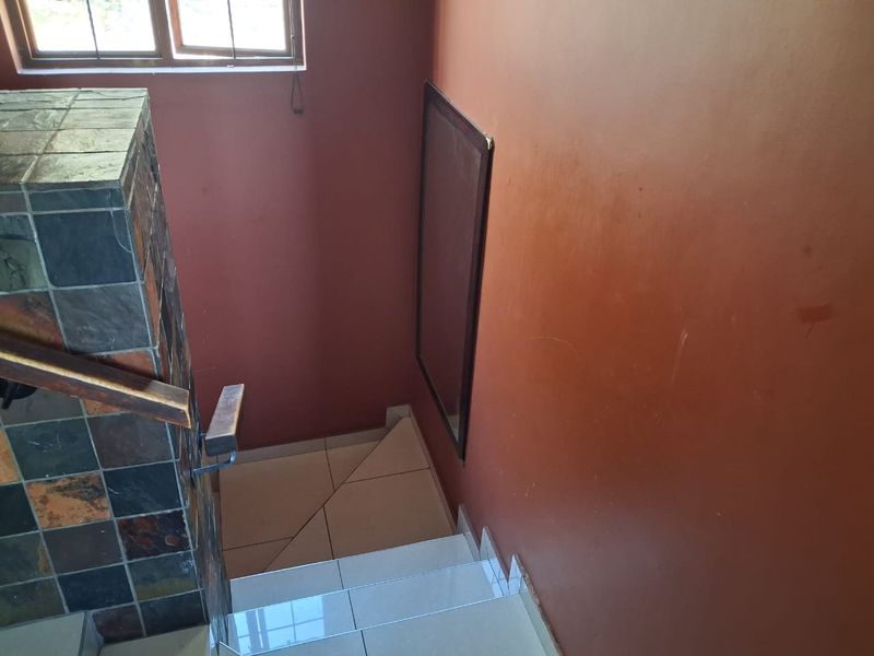 A staircase featuring tiled steps, a slate-clad pillar, and a wooden handrail, leading down to a lower level with terracotta-colored walls.