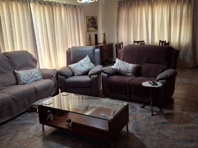 A living room featuring tiled flooring and a suspended ceiling grid, providing a functional and dated living space.