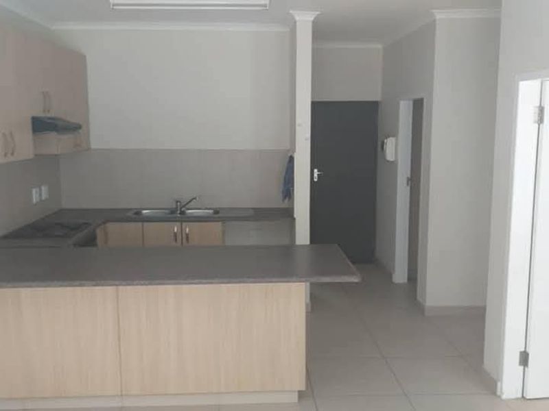 A functional, empty kitchen featuring light wood-finish cabinetry, laminate countertops, a built-in hob, and tiled flooring in an open-plan layout.