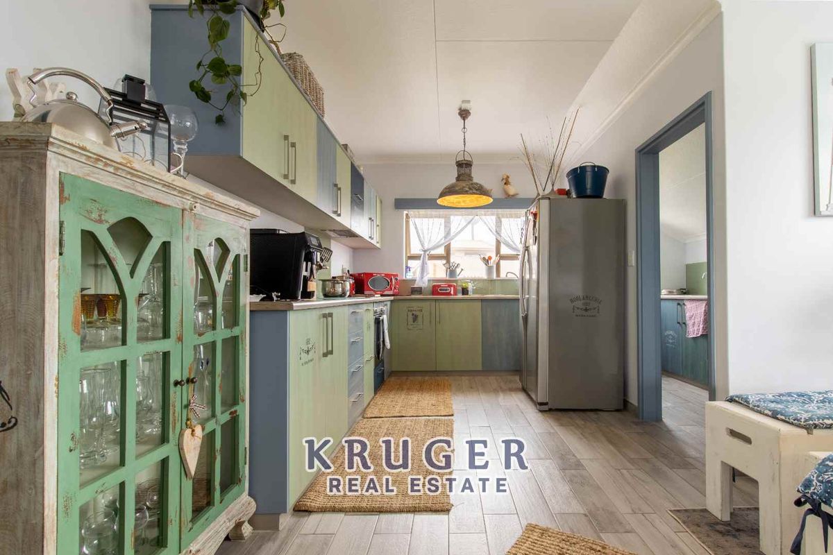 A functional kitchen featuring two-tone cabinetry, wood-look tile flooring, and a window providing natural light, with an adjacent doorway leading to a secondary space.