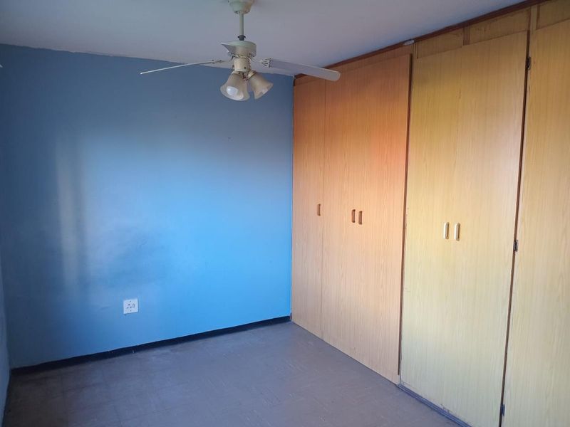 An empty bedroom featuring built-in wooden cupboards, a ceiling fan, and blue accent wall, requiring minor cosmetic updates to refresh the space.