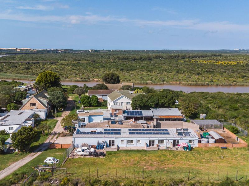 Aerial view of the property showing multiple buildings, solar panel installations, water tanks, and surrounding rural landscape near a river.
