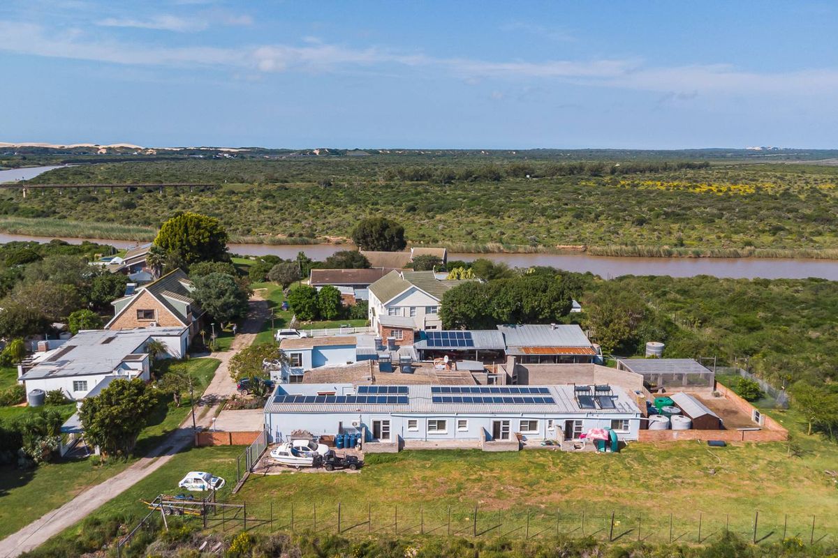 Aerial view of the property showing multiple buildings, solar panel installations, water tanks, and surrounding rural landscape near a river.