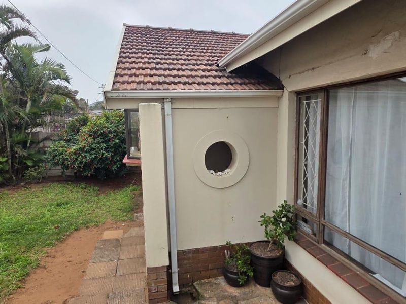 Rear exterior view of the house featuring a tiled roof, circular window detail, and a small garden area with paved walkway.