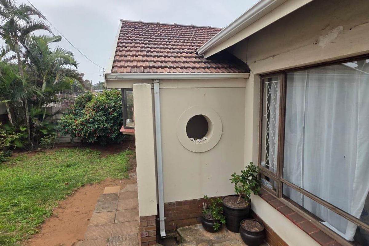 Rear exterior view of the house featuring a tiled roof, circular window detail, and a small garden area with paved walkway.