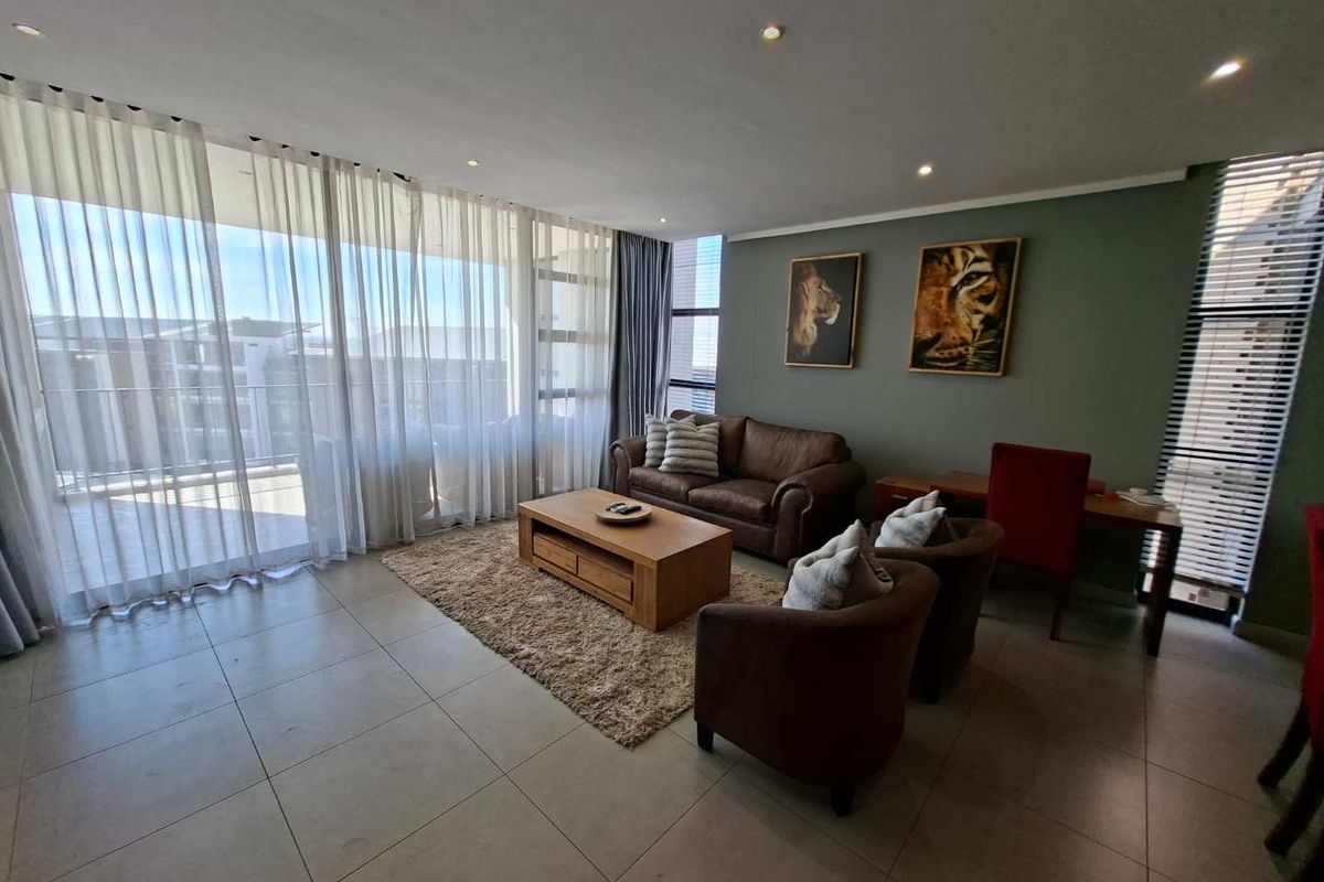 A well-lit living room featuring large sliding glass doors, neutral tiled flooring, and recessed downlighting, creating a bright and comfortable living space.